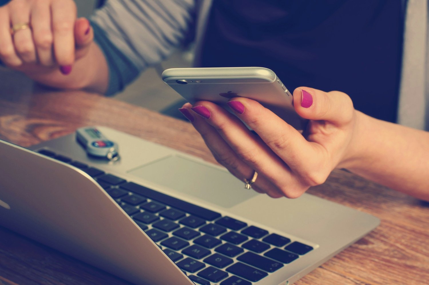 Mani che tengono uno smartphone davanti a un portatile