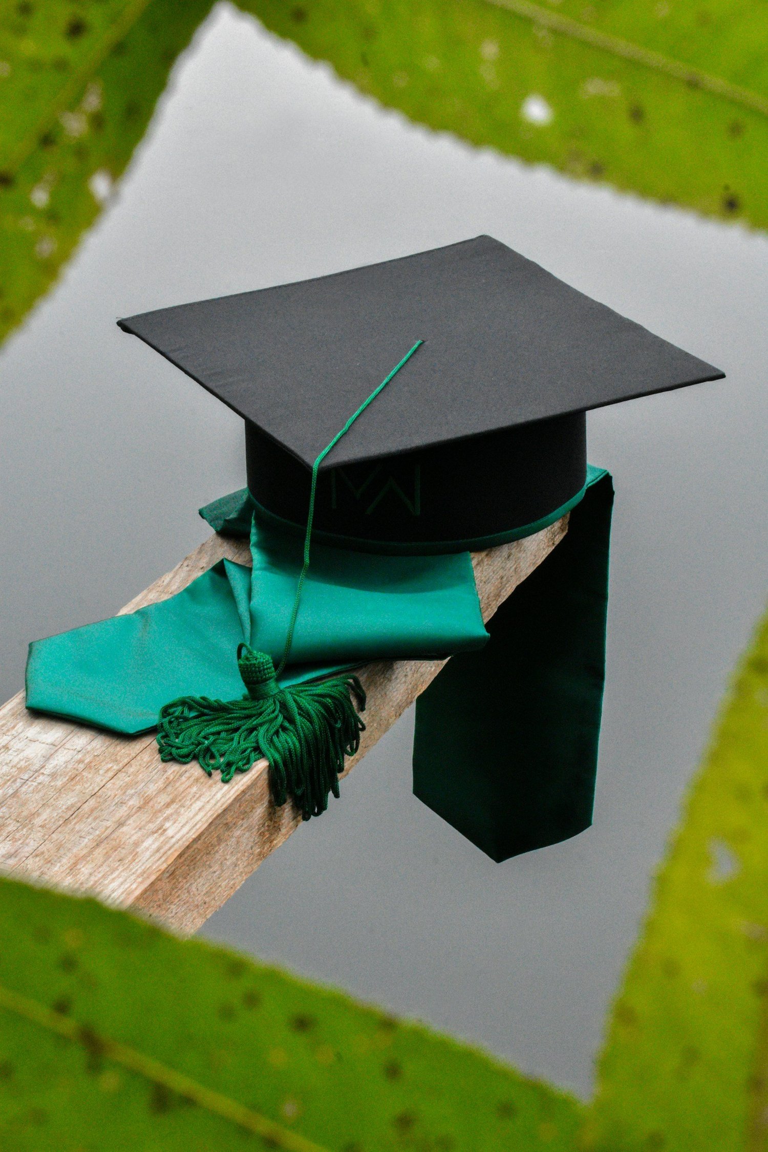 Tocco da laurea con stola verde appoggiato su una trave di legno